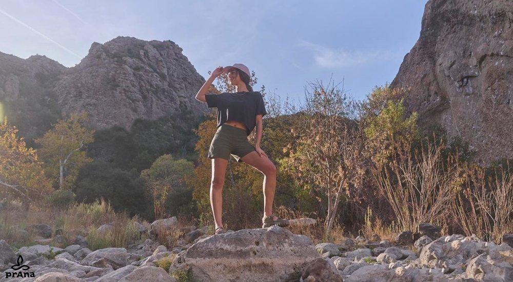A woman stands on rocky terrain wearing prAna Koen shorts