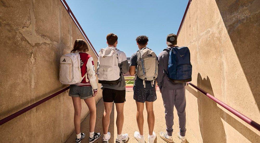 four students with backpacks in a football field tunnel
