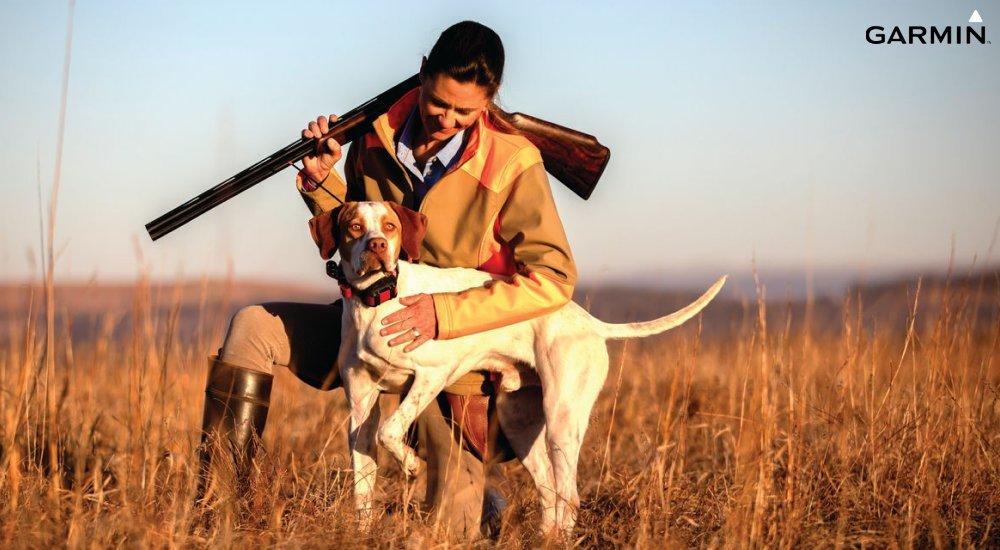 a hunter with a rifle by her dog in an ecollar