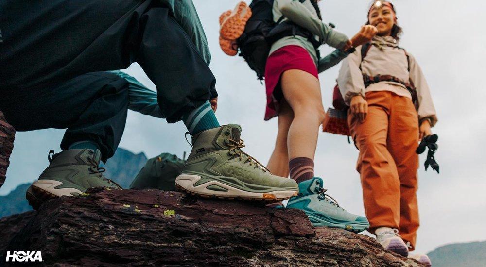 Three hikers standing on a rocky overlook in Hoka hiking boots