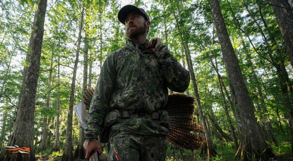 a hunter walking through the forest with a gun and a turkey