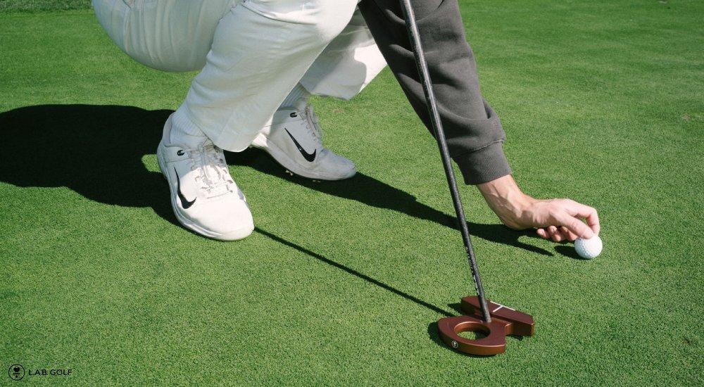 A golfer kneels holding a L.A.B. Golf putter