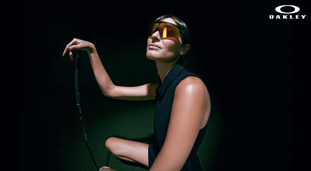 a woman holding a golf club wearing her oakley sunglasses