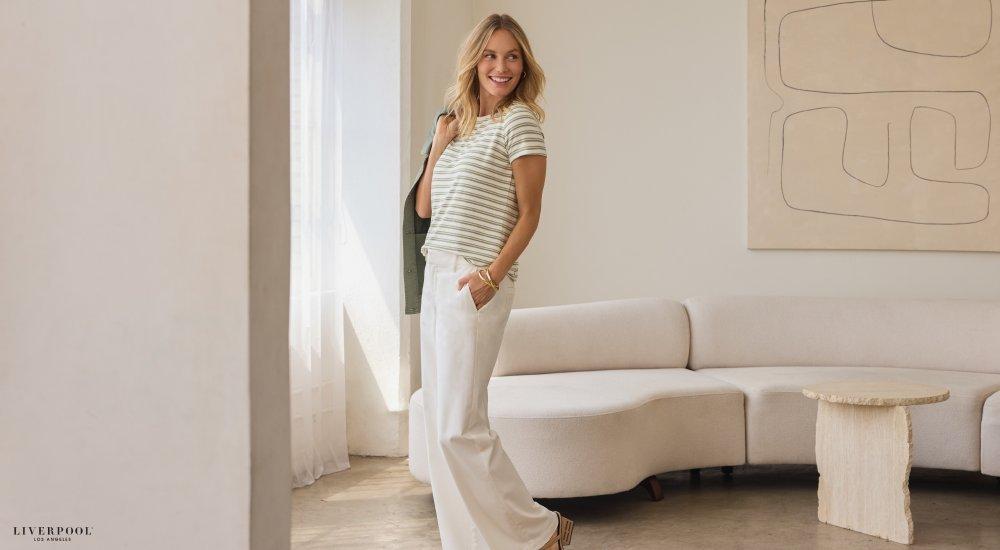 A woman wearing white pants and a simple t-shirt with a jacket over her shoulder