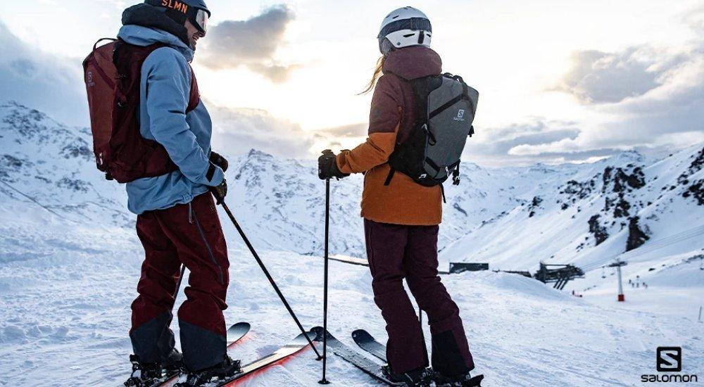 two people at the top of a hill, ready to ski down a mountain