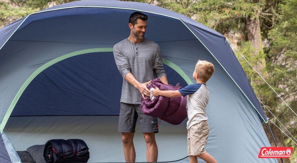 a son handing off a sleeping bag to his father while in a camping tent