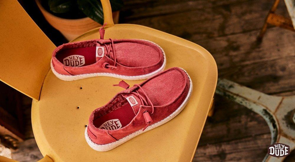 A red pair of Heydude shoes on a yellow chair