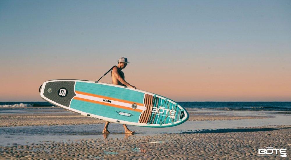 man carrying a standup paddle board across the beach
