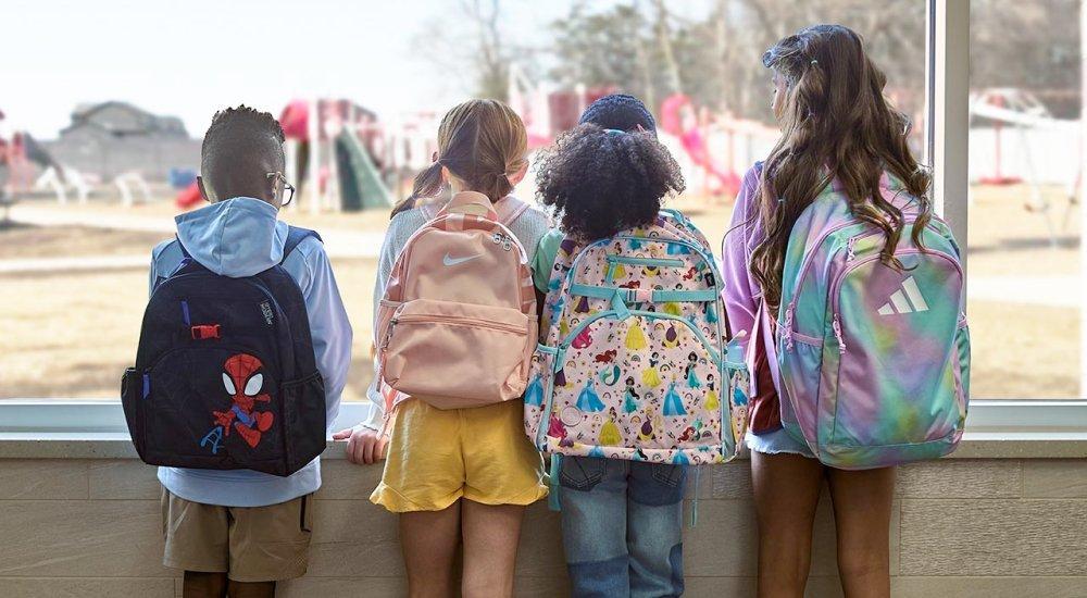 four kids wearing backpacks looking out the window