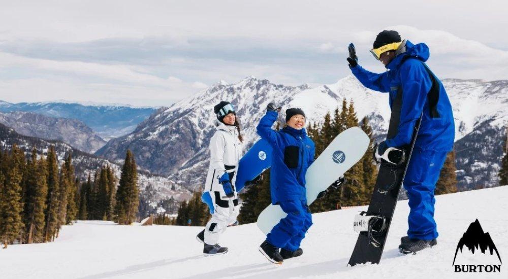 a kid giving another person a high five on the slopes with his snowboard
