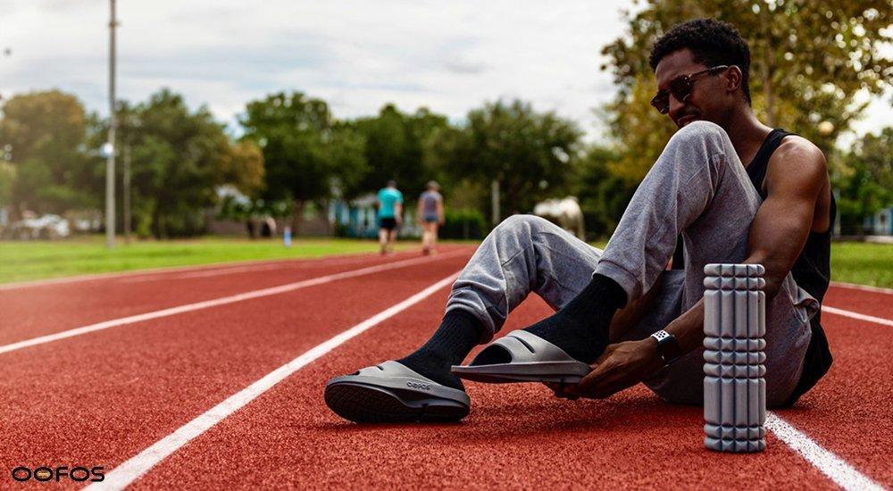 person sitting on the ground wearing OOFOS recovery shoes