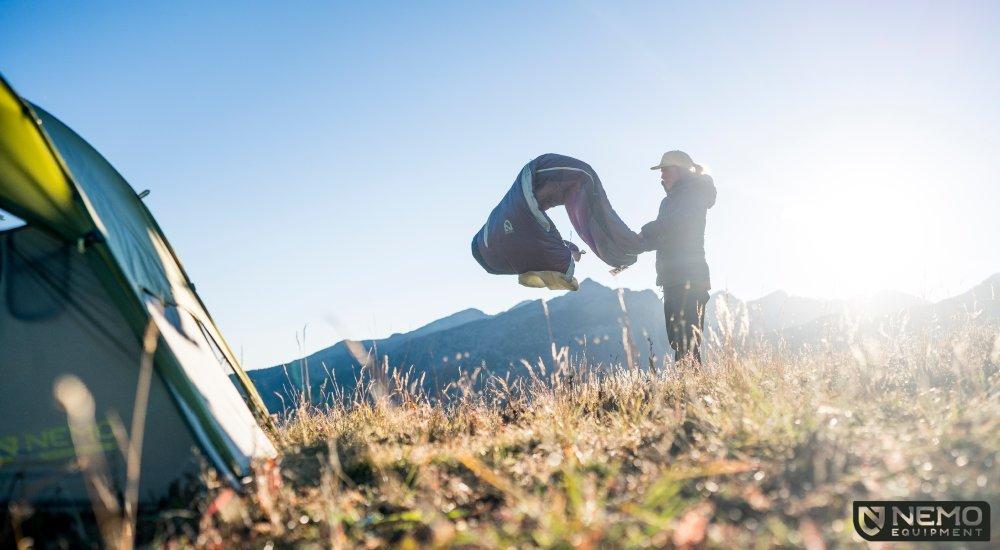 a woman shaking out a sleeping bag in the mountains