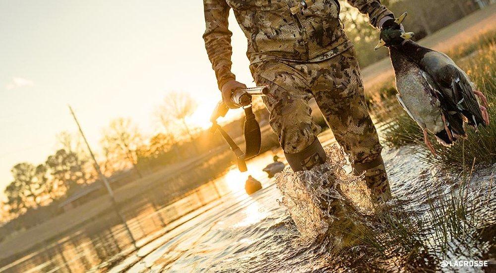a hunter carrying geese through the water in waders