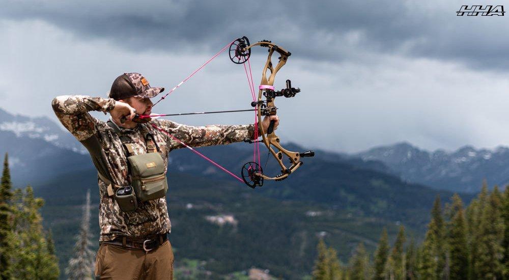 a man shooting his bow in the mountains using a bow sight