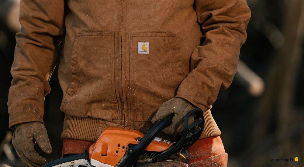 A worker with a chainsaw wears a Carhartt work jacket