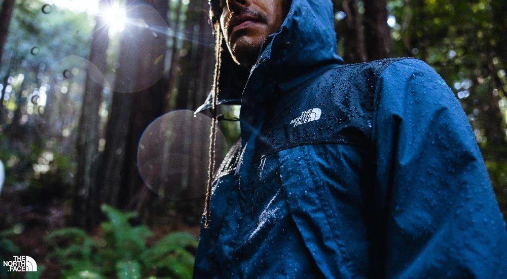 a man walking through the rain forest with a north face jacket