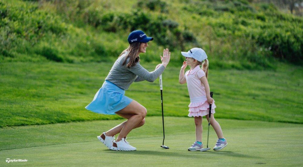 A woman golfer and a young girl golfer high five on a golf course