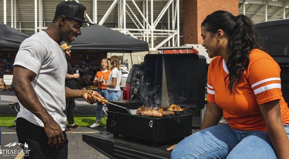 people tailgating in the parking lot and grilling with a Traeger grill