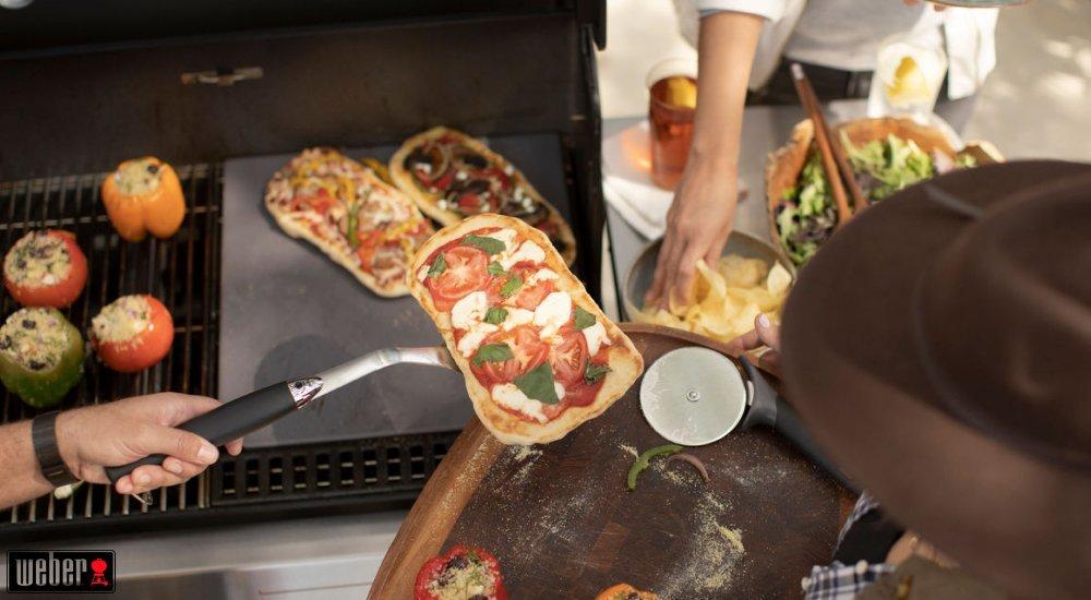 a person taking a pizza off a weber grill