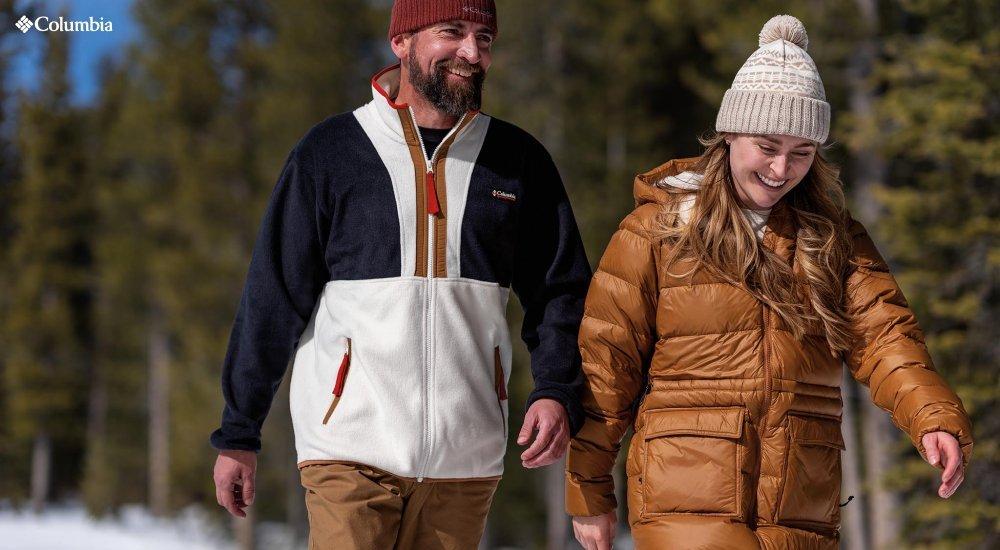 Man and woman walk in a snowy and tree-lined landscape