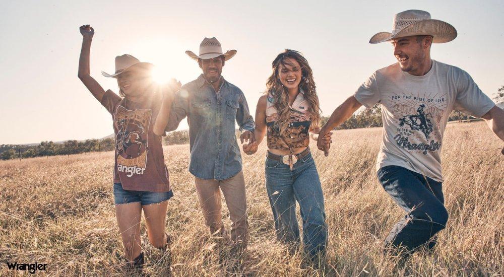 A group of people frolic in a field wearing Wrangler Western wear