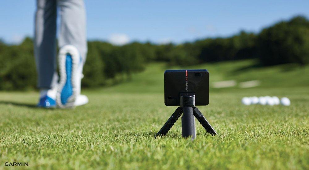 A Garmin golf launch monitor with a golfer and some golf balls in the background