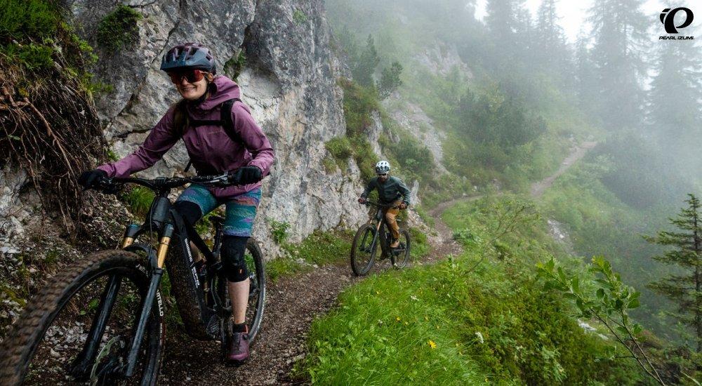 A female and male mountain biking on a misty forest trail along cliffs