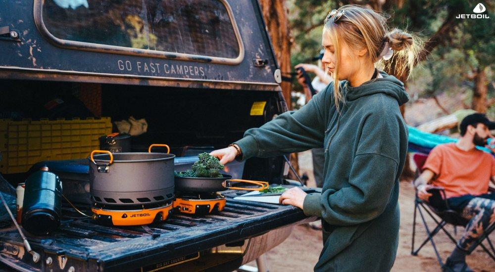 a woman cooking with a Jetboil stove on the back gate of her pick-up truck in a campground