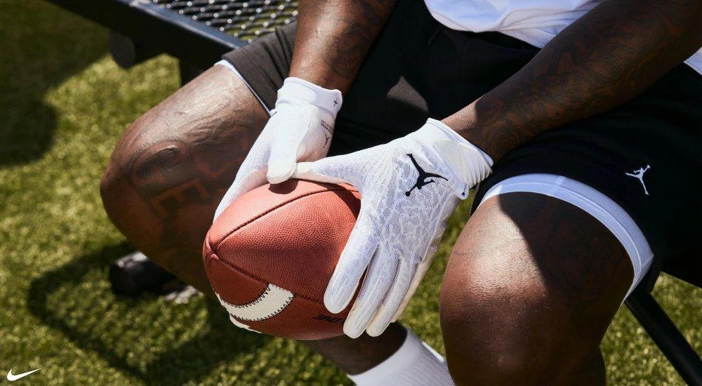 a player wearing Jordan football gloves and holding a football while sitting on a bench