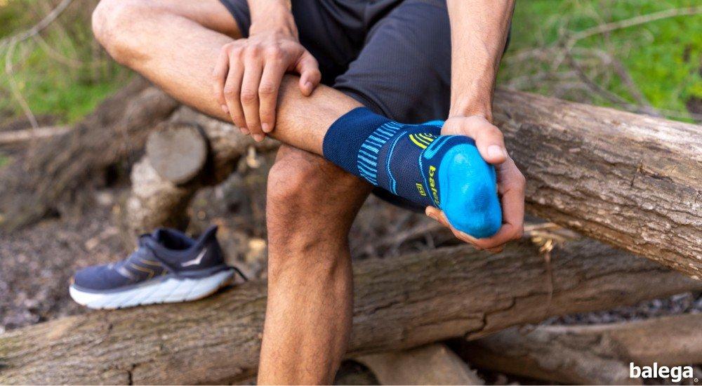 a guy putting on a running sock while sitting on a log