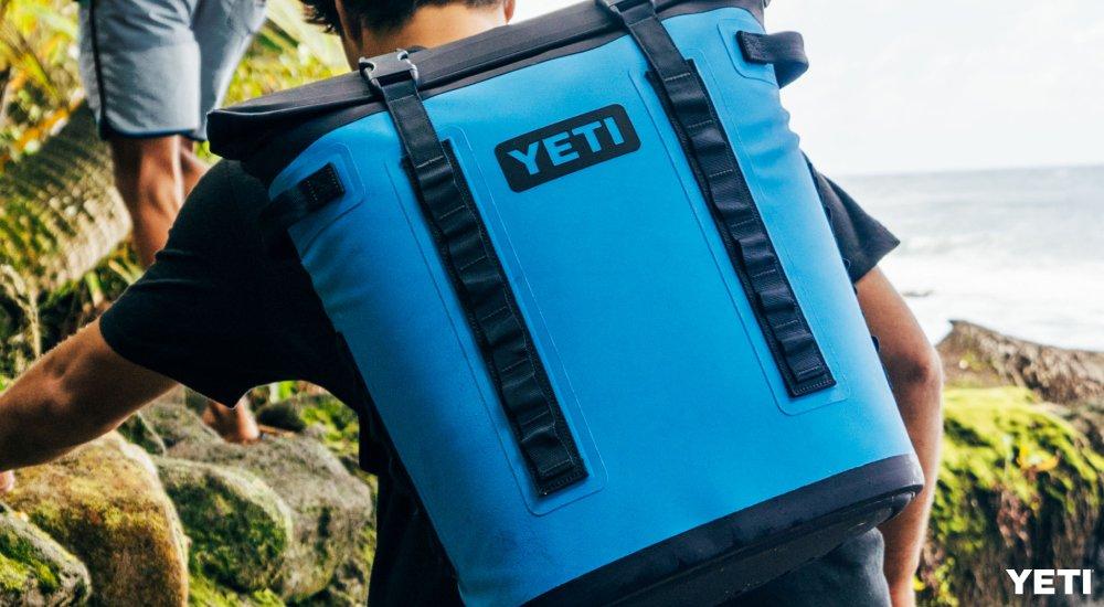 a guy climbing up a hill with a yeti soft cooler on his back