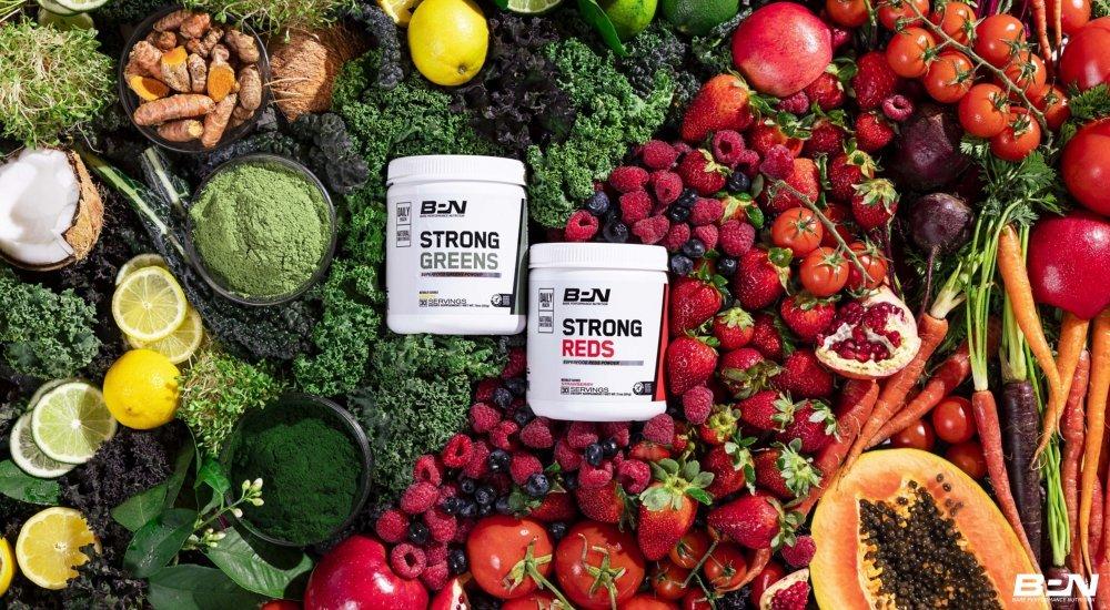 BPN Greens and Reds powders with a background of vibrant fruits and vegetables