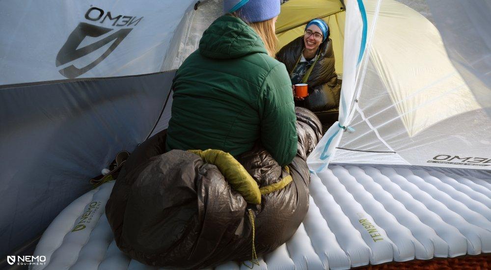 Two women hanging out and chatting over some coffee while sitting on their sleeping pads