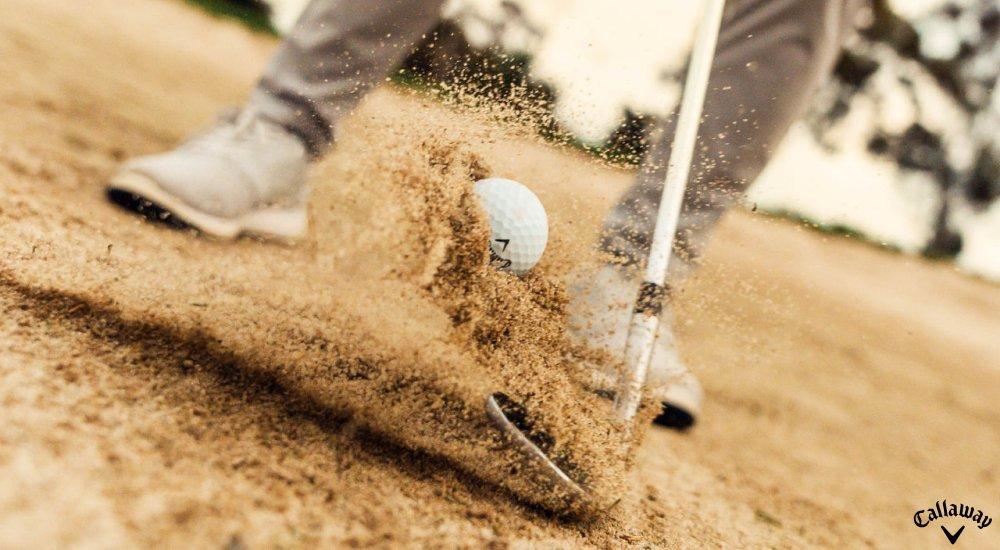 Swinging a golf club through a sandy bunker