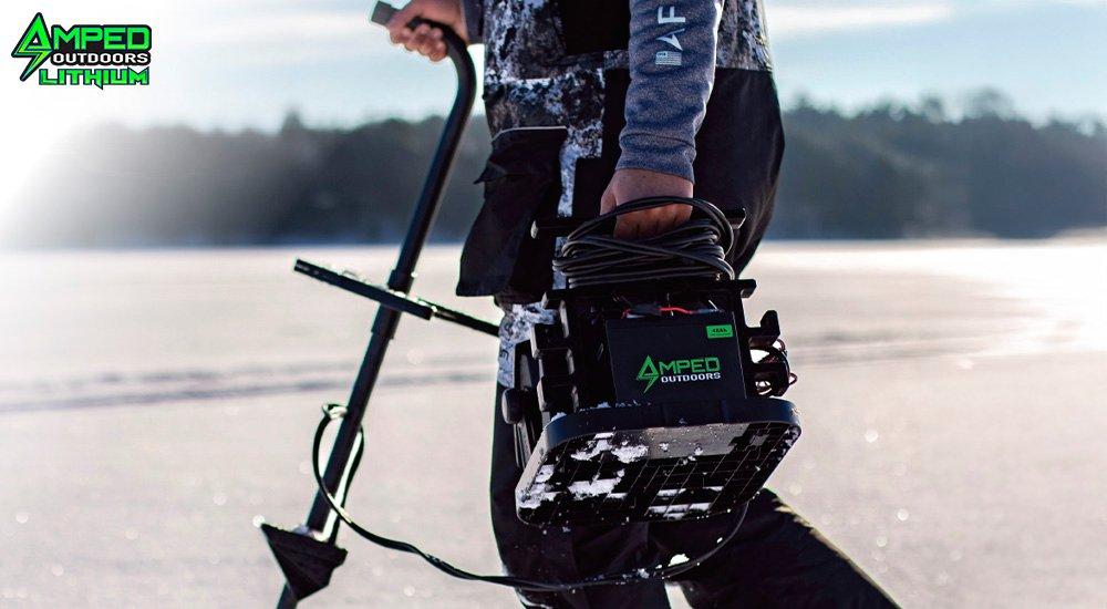 an ice angler holding an amped outdoors battery in a shuttle with forward facing sonar 