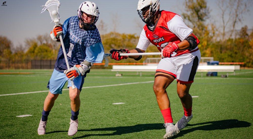 two players playing lacrosse while wearing all their gear