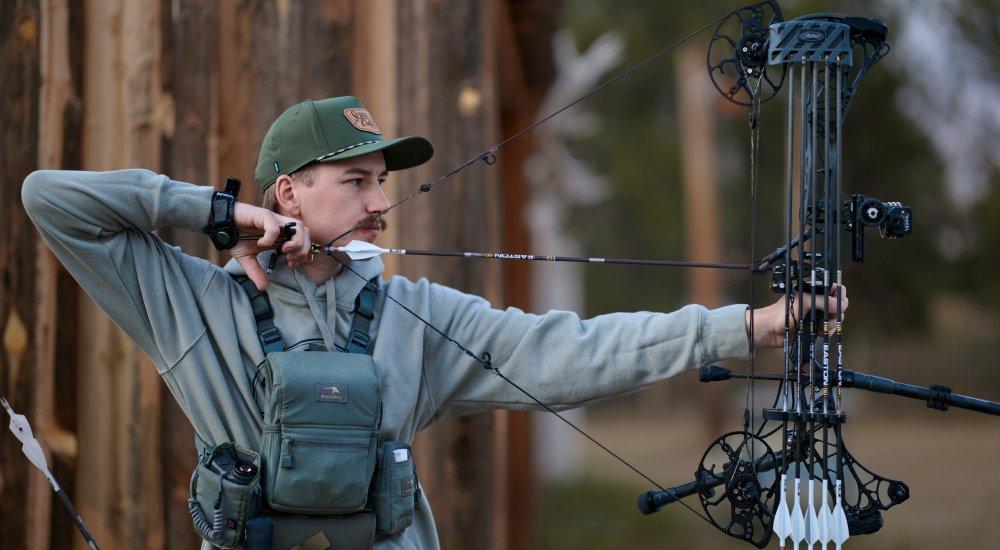 a man shooting his bow in the mountains using a bow sight