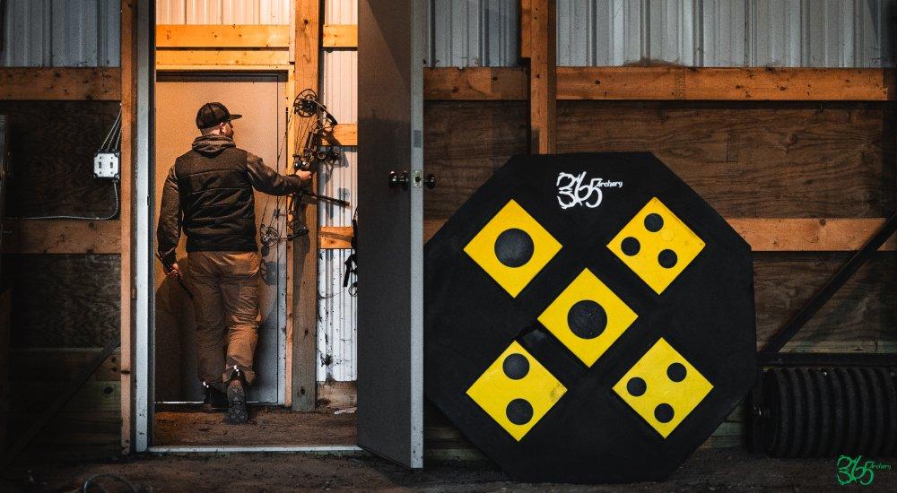 an archery target resting by a shed while the hunter hangs up his compound bow