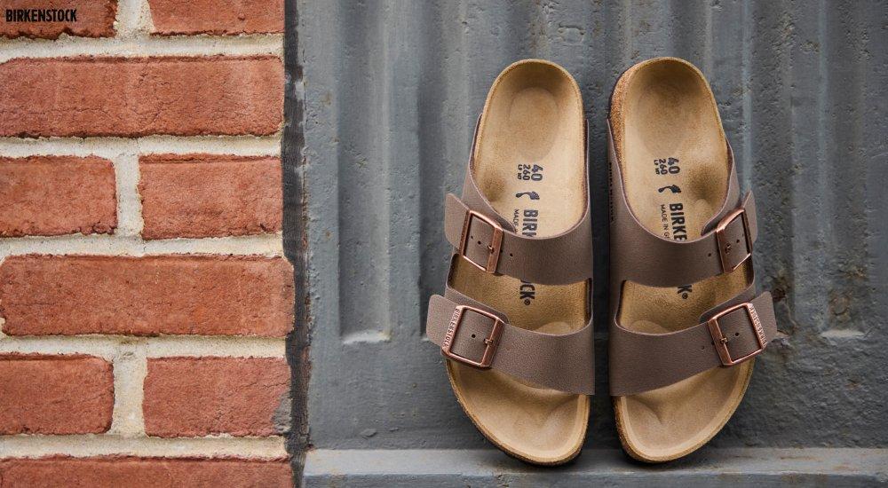 a pair of Birkenstock Arizona sandals next to a brick wall