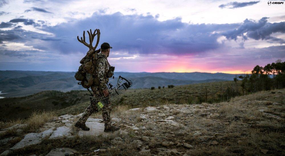 a hunter walking through water while holding a compound bow