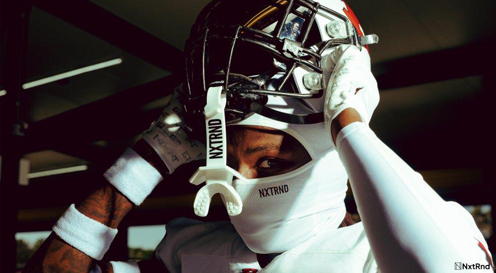 man lifting football helmet off their head. mouthguard is dangling in front of them.