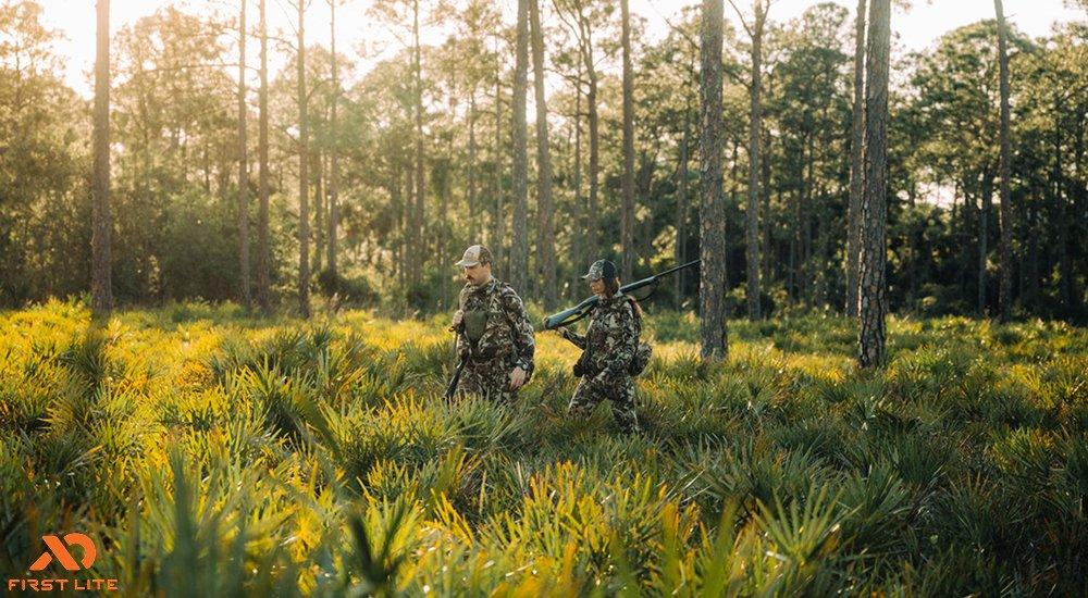 two hunters walking through bushes and trees