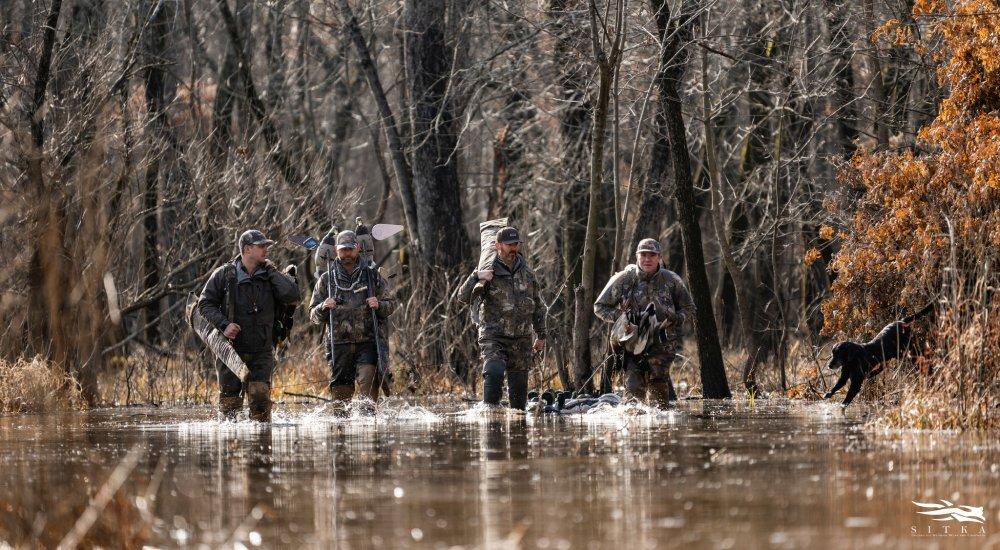 four hunters wading through water