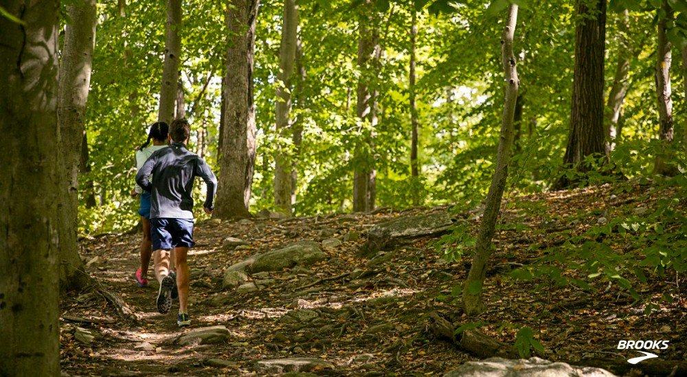 two people running in the woods on a trail