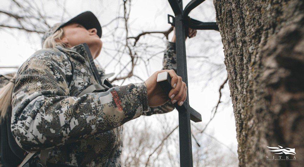 a female hunter climbing up a ladder wearing hunting clothing