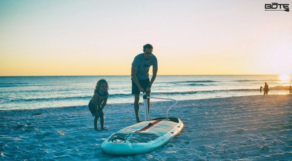 guy and kid inflating an inflatable stand up paddle board on the beach