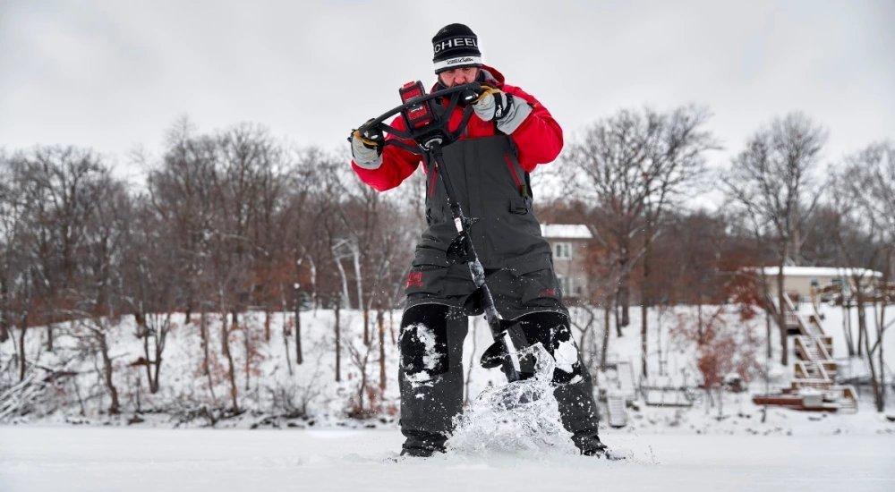 an angler using an ice auger to drill a hole on the lake