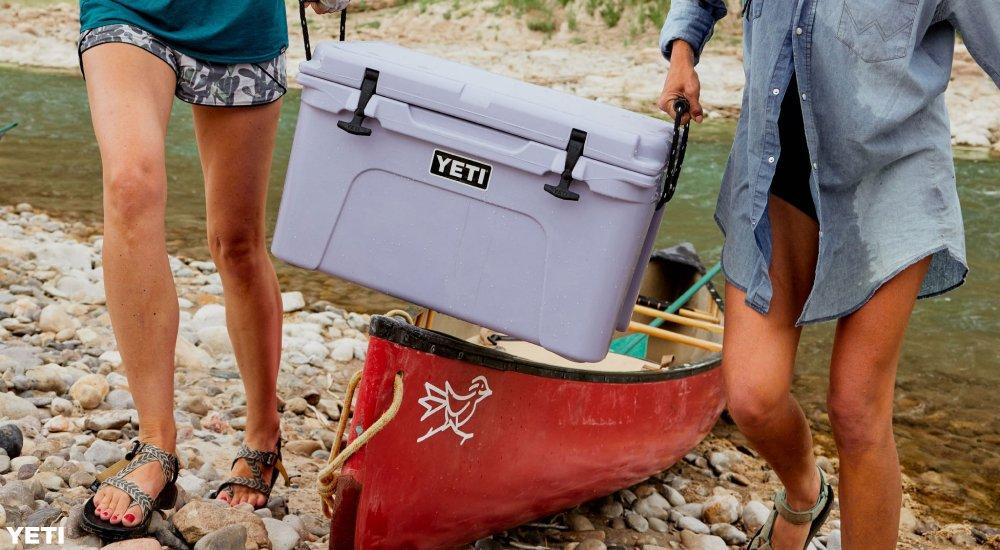 two women carrying their yeti cooler off of a kayak on a beach