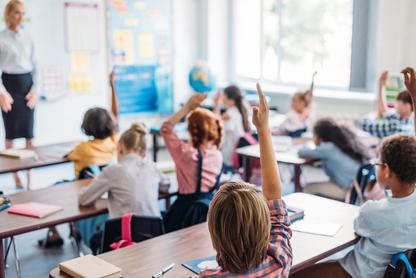 Kids in a classroom, one child raising their hand