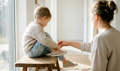 Child sitting on a bench while Mom helps them put on a pair of shoes